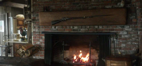 Large Fireplace in the Dolphin House - rifle mounted above it on the brick, firewood beside it and pot on the other side